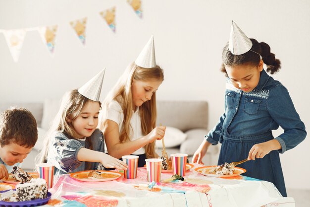 Детский веселый день рождения в украшенной комнате. Счастливые дети с тортом и баллонами.
