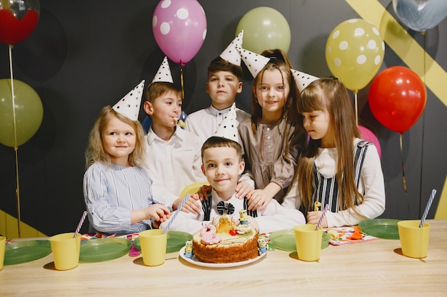 Children's funny birthday party in decorated room. Happy kids with cake and ballons.