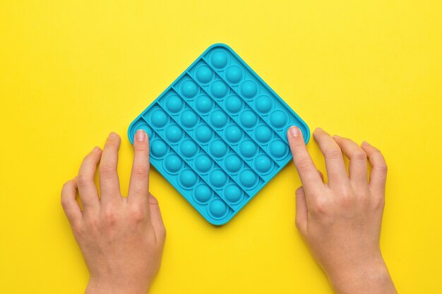 Детские руки с силиконовой игрушкой pop it на желтом фоне. популярный антистрессовый продукт.