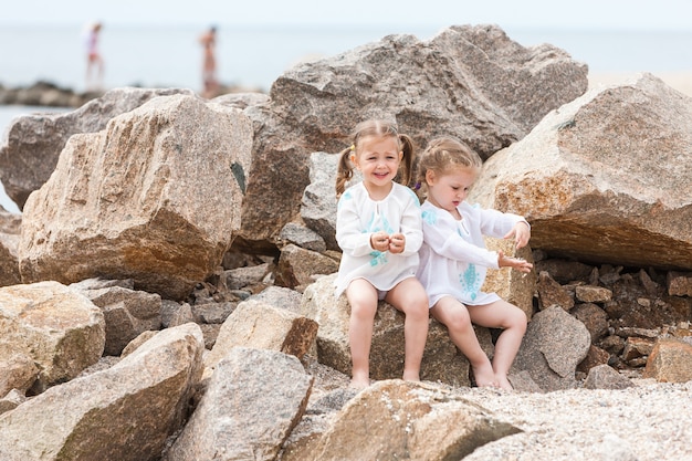 Дети на морском пляже. Близнецы сидят на фоне камней и морской воды.