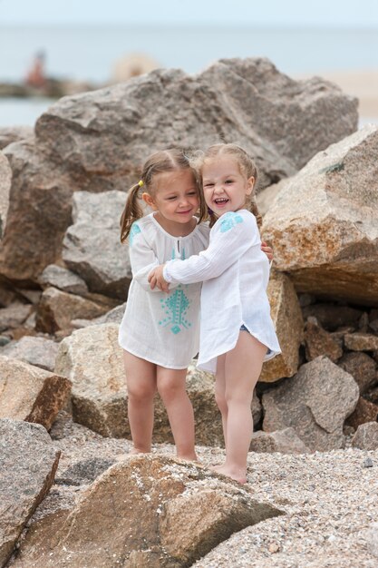 Children on the sea beach. Twins standing against stones and sea water.