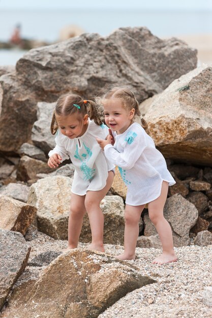 Children on the sea beach. Twins standing against stones and sea water.