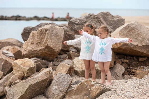 海のビーチで子供たち。双子が石と海の水に立ち向かいます。