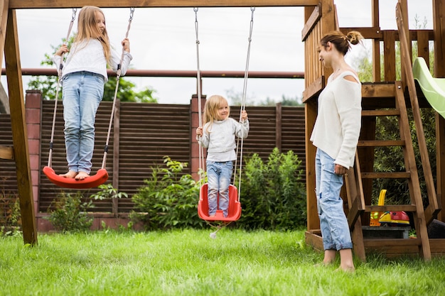 ブランコに乗っている子供たち。女の子の姉妹は庭のブランコに揺れています。夏のお楽しみ。