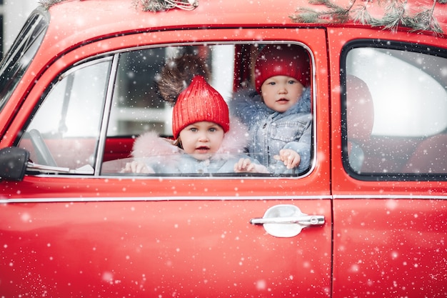 Children in warm clothes bask in a red car during snowfall