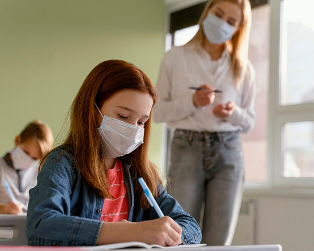 女教師と学校で学ぶ医療マスクを持つ子供たち