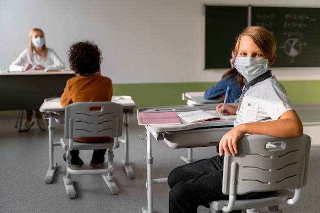 Children with medical masks learning in school with female teacher