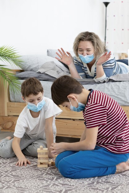 Children with medical masks playing jenga at home with mother