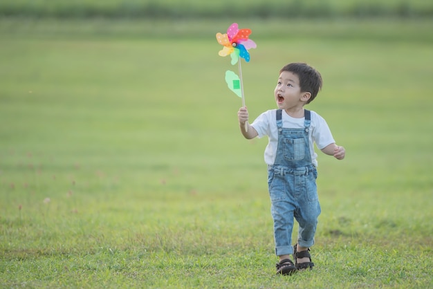 Детская красочная игрушка ветряк. смеющийся ребенок счастливо играет. Маленький мальчик дует летом в летнем лагере на солнышке против красочной ветряной мельницы.
