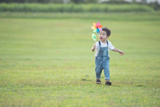 子供のカラフルな風車のおもちゃ。楽しそうに笑う子供。夏の夏の日差しの中で、小さな男の子が色とりどりの風車にぶつかる。