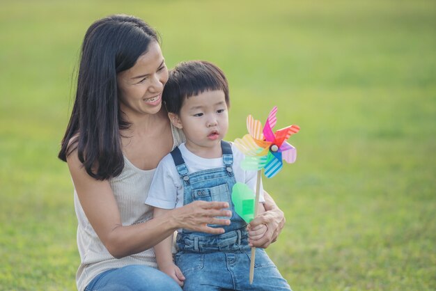 子供のカラフルな風車のおもちゃ。楽しそうに笑う子供。サマーキャンプで夏に小さな男の子がカラフルな風車にぶつかる。女性と小さな男の子が遊んでいます。