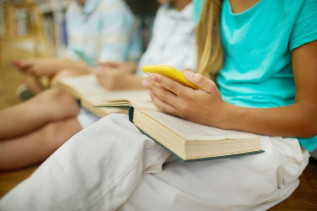 Childrens hand holding smartphone over open book