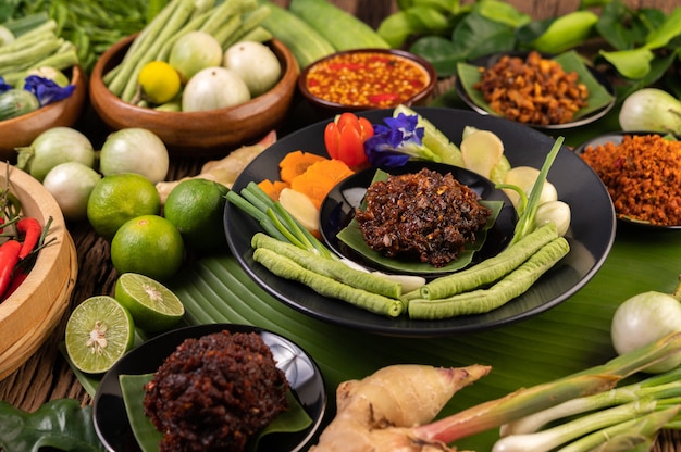 Chili paste is served on banana leaves on a plate with long beans, lime, chili, and eggplant.