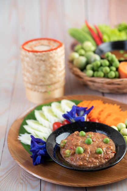 Chili paste paste in a bowl with eggplant, carrots, chili, cucumbers in a basket on wood table