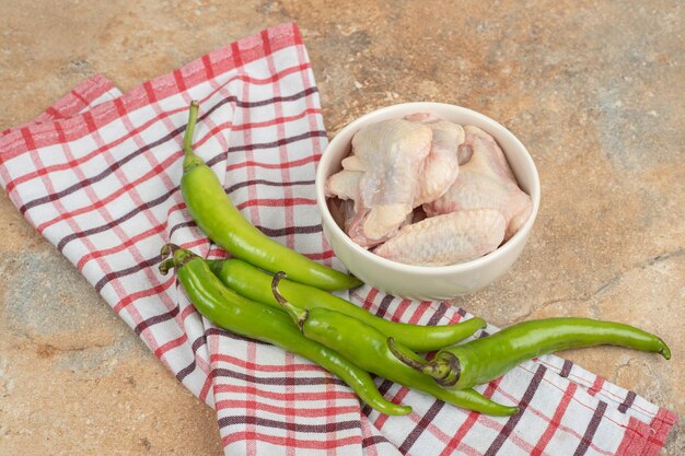 Chili peppers with unprepared chicken legs on tablecloth