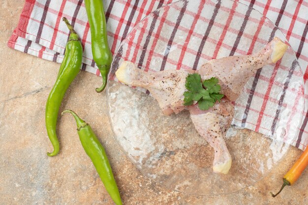 Chili peppers with unprepared chicken legs on tablecloth