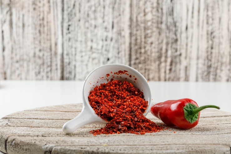 Free Photo chili powder with red pepper and wooden piece in a white scoop on white and wooden grunge wall, side view.