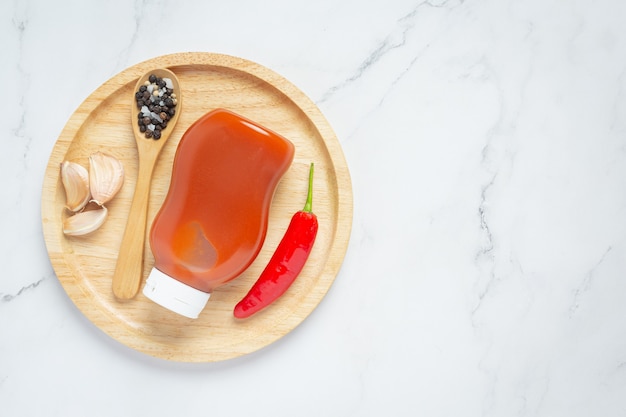 Chili sauce in bottle and peppers on wooden surface