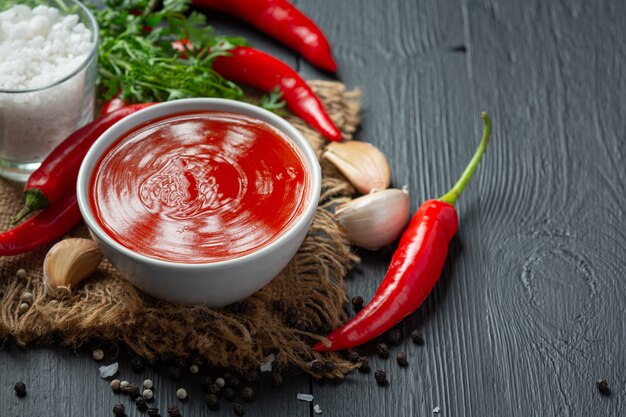 Chili sauce and peppers on dark wooden surface