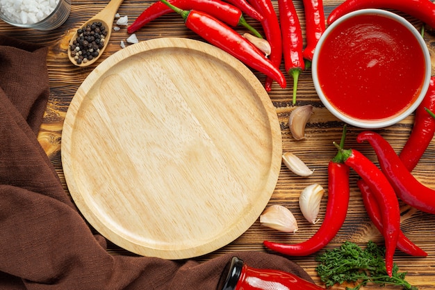 Chili sauce and peppers on wooden surface