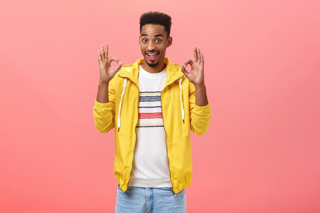 Chill guys I got it. Portrait of happy stylish and cool african american with afro hairstyle in trendy yellow jacket raising ok or okay gesture hearing excellent idea over pink background