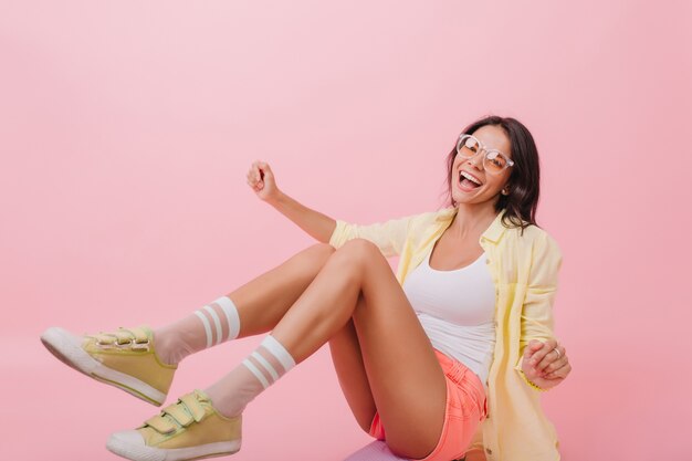 Chilling girl in cute yellow sneakers sitting on the floor. Lovable european brunette woman in bright outfit relaxing