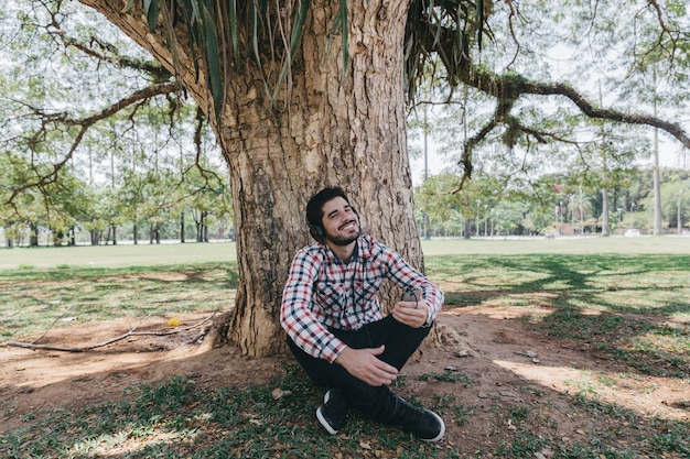 Foto gratuita uomo di refrigerazione in cuffie sotto l'albero