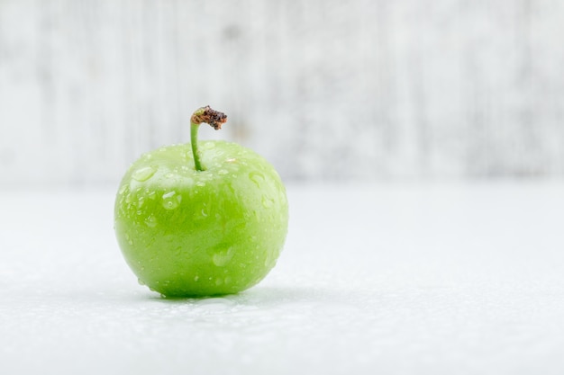 Chilly green plum on grungy and white wall. side view.