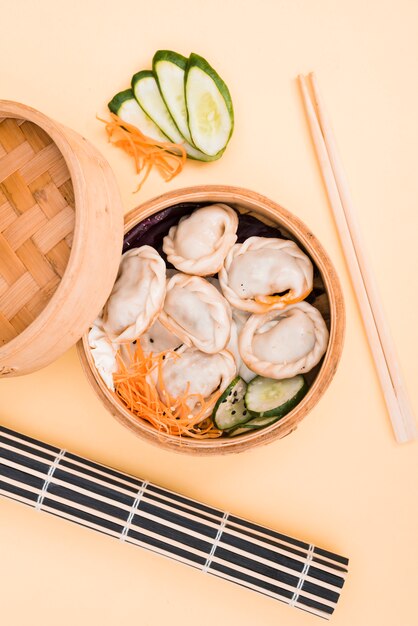 Chinese dumpling and salad in a bamboo steamer box on colored backdrop with chopsticks