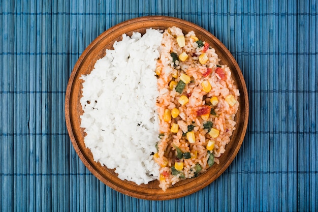 Chinese fried and steamed rice on wooden plate over the blue placemat