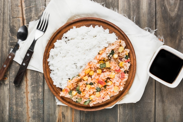 Chinese fried and steamed rice on wooden plate with soya sauce over the table