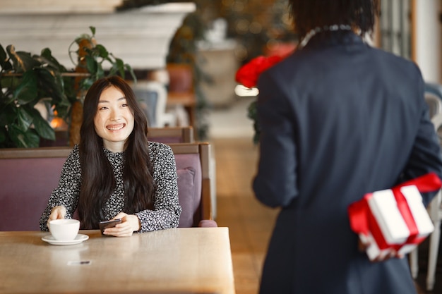 Chinese girl with phone. Black guy is preparing a surprise. Happy girl at the table