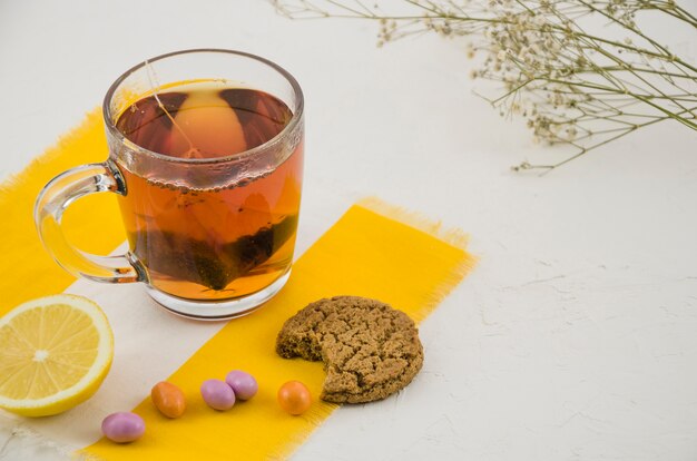 Chinese herbal tea cup with candies and eaten cookies on white background with gypsophila twig