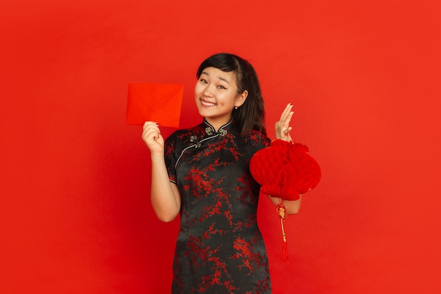무료 사진 중국 새 해 2020. 빨간색 배경에 고립 된 아시아 젊은 여자의 초상화. 전통적인 옷을 입은 여성 모델은 장식과 빨간 봉투에 행복해 보입니다. 축하, 휴일, 감정.