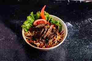 Free photo chinese noodles inside bowl with chopped steak, tomato slices and lettuce.