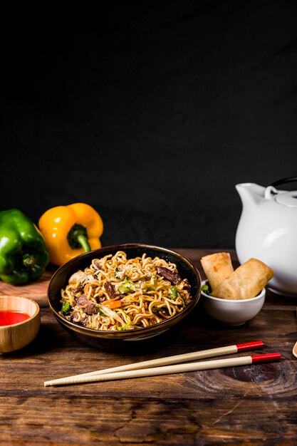 Chinese noodles with beef and vegetables served with spring rolls on wooden desk