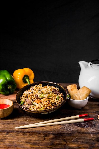 牛肉と野菜の中華麺、木製の机の上の春巻きを添えて