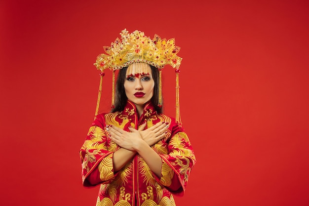無料写真 赤い背景の上のスタジオで中国の伝統的な優雅な女性。民族衣装を着た美少女。中国の旧正月、優雅さ、優雅さ、パフォーマー、パフォーマンス、ダンス、女優、ドレスのコンセプト