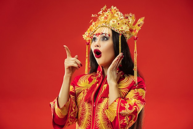 赤い背景の上のスタジオで中国の伝統的な優雅な女性。民族衣装を着た美少女。中国の旧正月、優雅さ、優雅さ、パフォーマー、パフォーマンス、ダンス、女優、ドレスのコンセプト