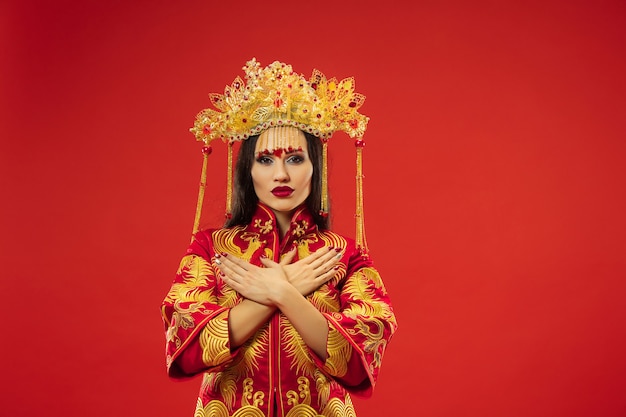 Chinese traditional graceful woman at studio over red background. Beautiful girl wearing national costume. Chinese New Year, elegance, grace, performer, performance, dance, actress, dress concept