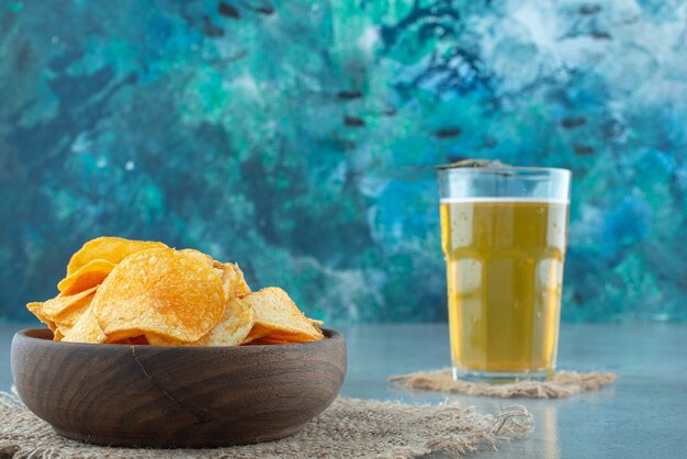 Chips in a bowl next to glass of beer , on the marble table. 