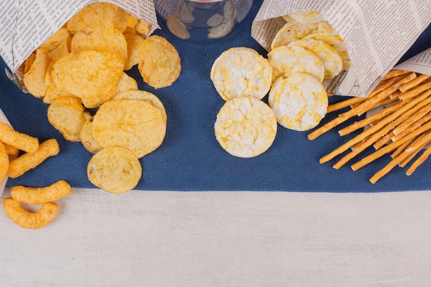 Chips, crackers and pretzels on blue tablecloth.