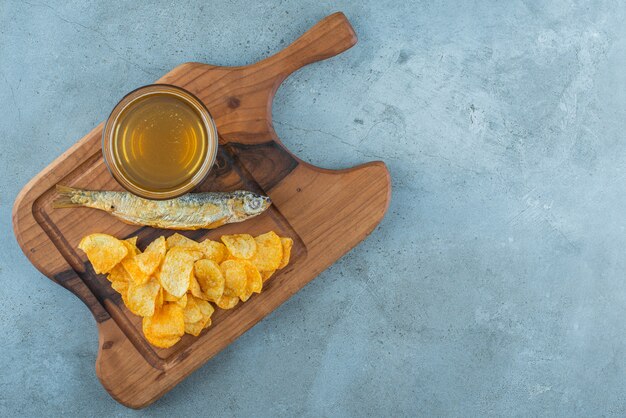 Chips, fish and glass of beer on board on marble.