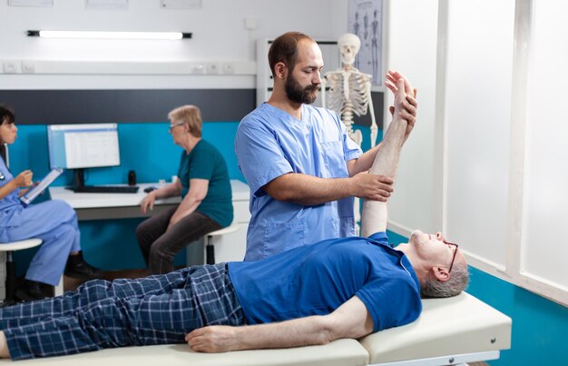 Chiroptractor doing osteopathic massage on aged patient for hand muscle recovery. Nurse giving assistance to stretch arm joint of senior man for osteopathy treatment and healthcare.