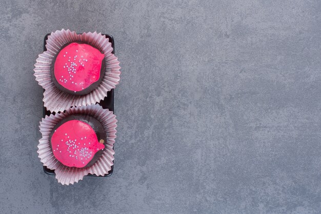 Шоколадные шарики с розовой глазурью на темной тарелке.