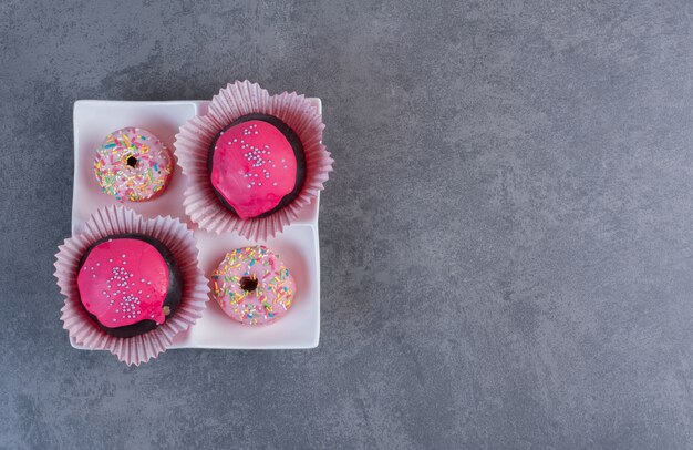 Chocolate balls with pink glaze and donuts on white plate.