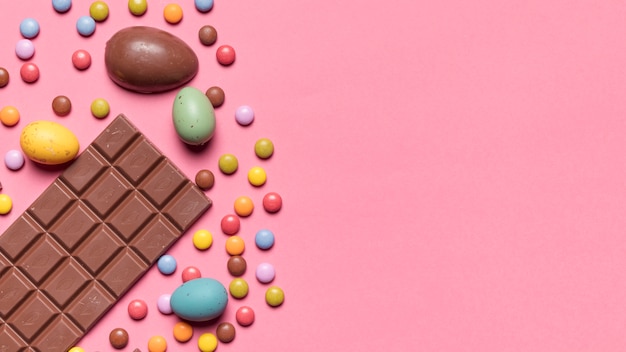 Free photo chocolate bar; easter eggs and gem candies on pink background