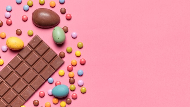 Chocolate bar; easter eggs and gem candies on pink background