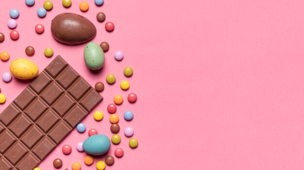 Плитка шоколада; пасхальные яйца и драгоценные конфеты на розовом фоне