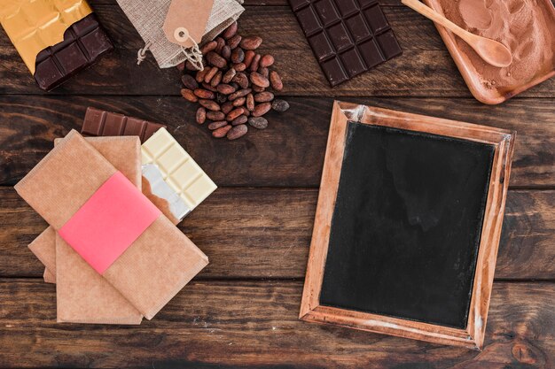 Chocolate bar stack, blank wooden slate, cocoa beans and powder on table